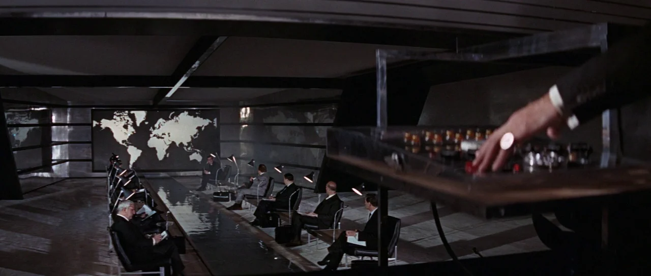 Thunderball (1965) movie still: wide — A dark, modern 1960s command center features rows of men seated at desks. A large illuminated world map glows…