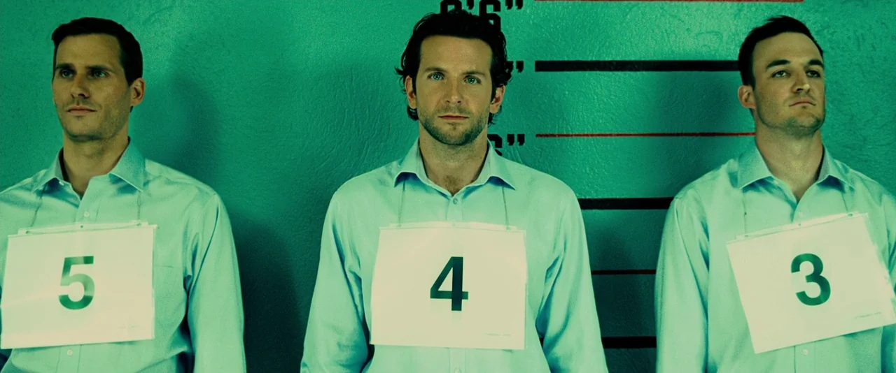 Limitless (2011) movie still: medium — A green wall with height measurements stands behind three men in matching shirts. Each man wears a white sign…