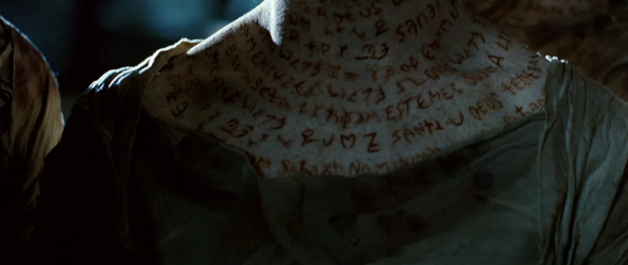 The Haunting in Connecticut (2009) movie still: closeup — A dimly lit interior space contains a person with visible writing on their skin. The…