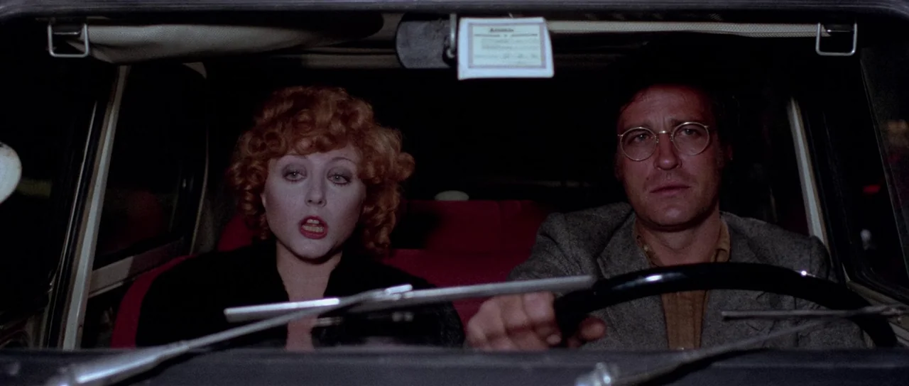 The Suspicious Death of a Minor (1975) movie still: medium — Two people sit inside the dark interior of a car at night. The man is behind the…