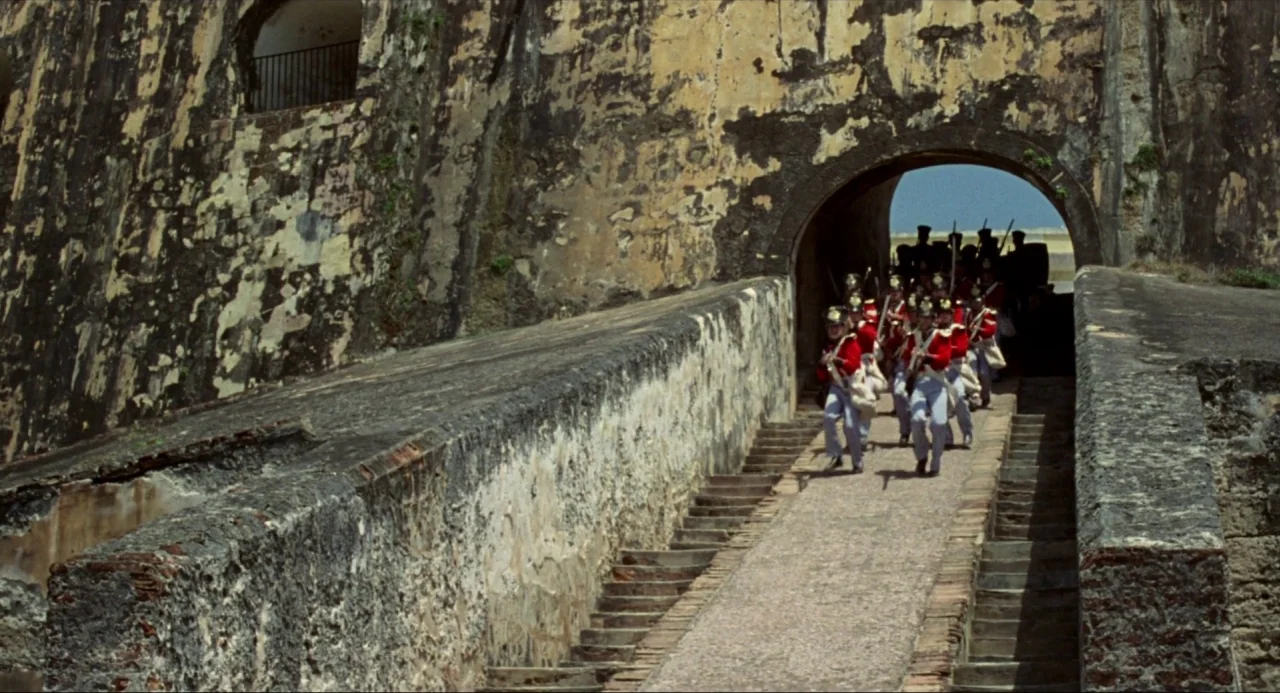 Amistad (1997) movie still: wide — A group of soldiers marches out of a dark stone tunnel of a fortress. The weathered stone walls show significant…
