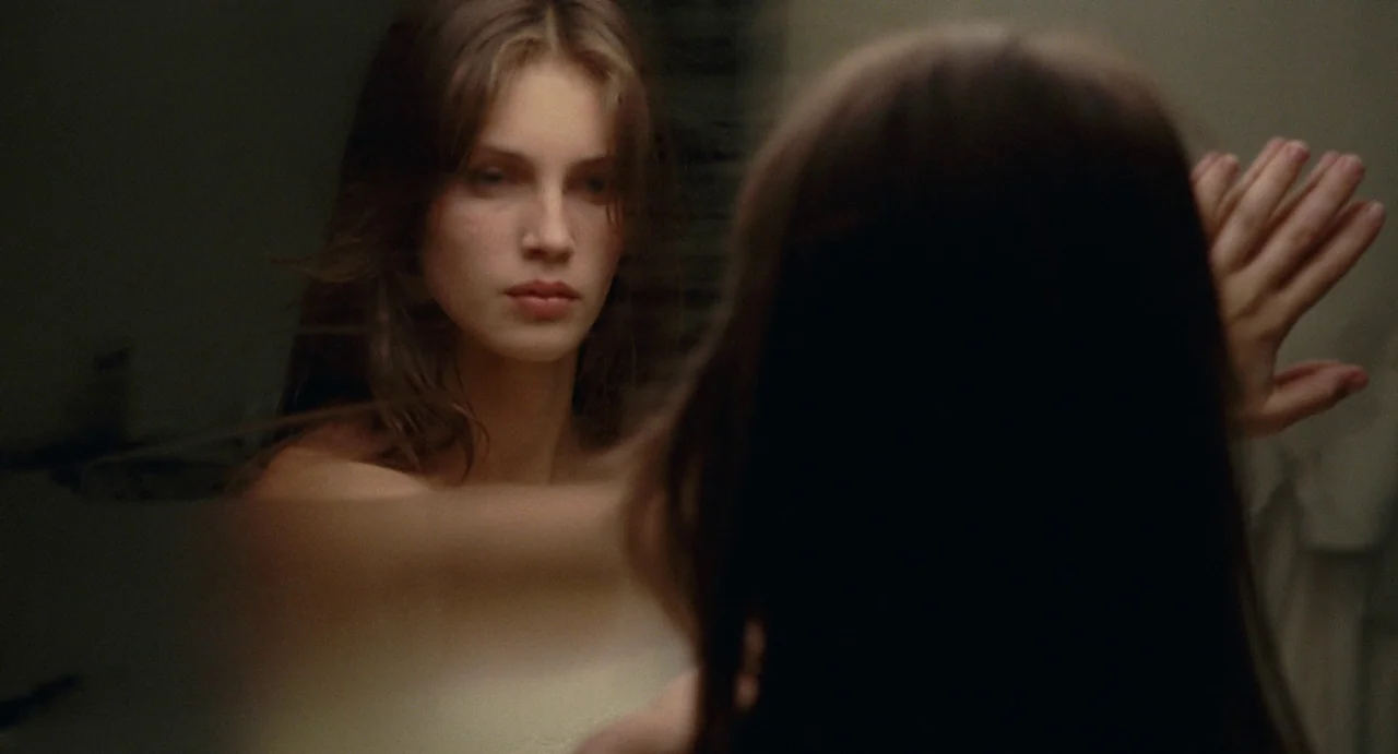 Young & Beautiful (2013) movie still: medium — A dimly lit room with a reflective glass surface and soft wall textures. A young woman touches the…