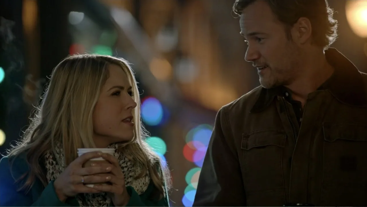 The Christmas Cure (2017) movie still: medium — A dark outdoor urban setting features blurred colored bokeh lights in the deep background. A man and…