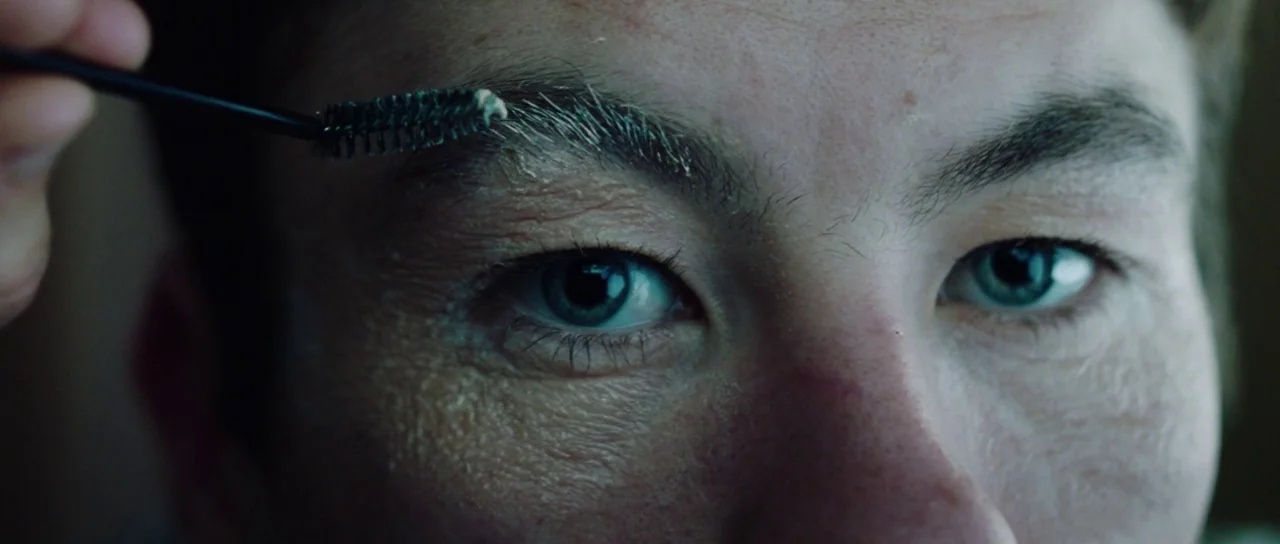 American Animals (2018) movie still: closeup — A close-up shot focuses on a person grooming their eyebrows. A spoolie brush applies a styling…