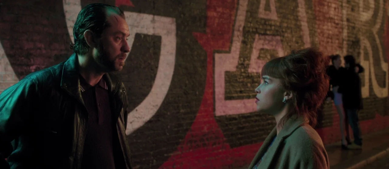 Dom Hemingway (2013) movie still: medium — A dark urban exterior features a brick wall painted with large white letters. A man and a woman stand…