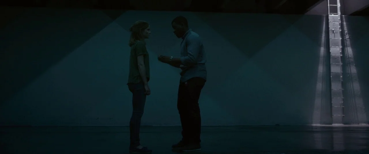 The Circle (2017) movie still: fullbody — A vast, empty concrete chamber with a steep metal ladder against the back wall. A woman and a man stand…