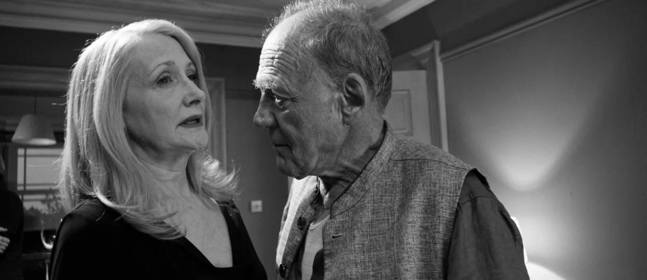 The Party (2017) movie still: medium — An interior space features two individuals engaged in a direct, close-proximity conversation. Soft light…