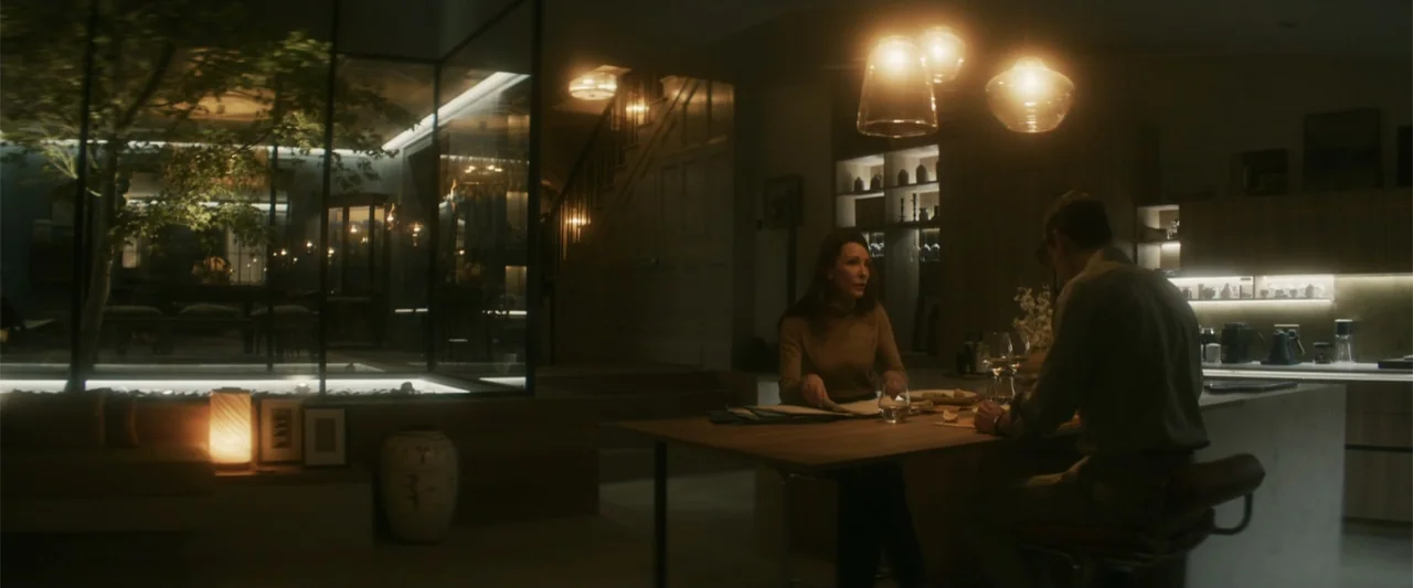 Black Bag (2025) movie still: wide — A dark modern house interior features a large central glass-walled atrium with a tree. A man and woman sit…