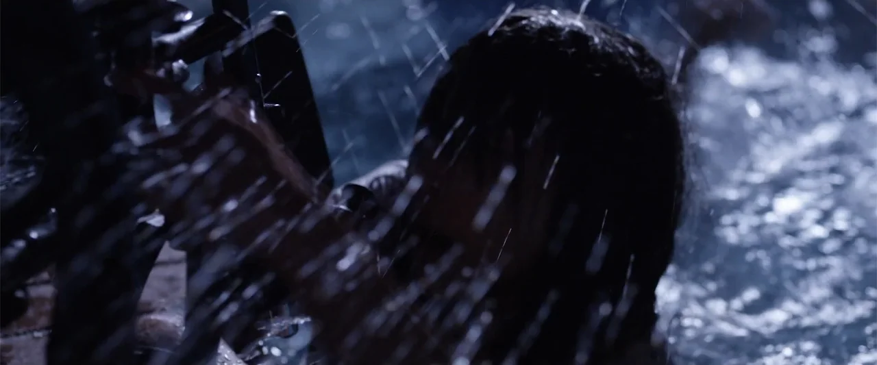 Mermaid Down (2019) movie still: closeup — A dark, wet urban environment features heavy rainfall obscuring the background. A person stands partially…