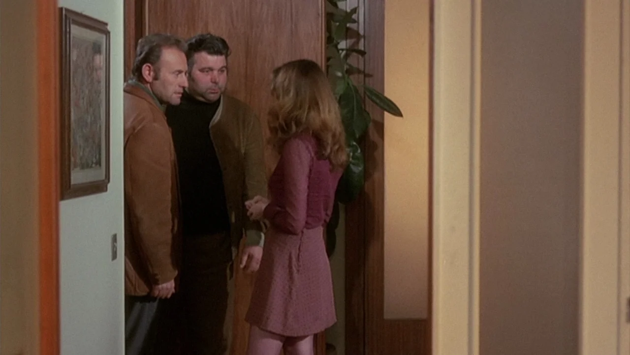 The Black Belly of the Tarantula (1971) movie still: fullbody — A residential hallway features wood paneling and a houseplant tucked into a corner.…