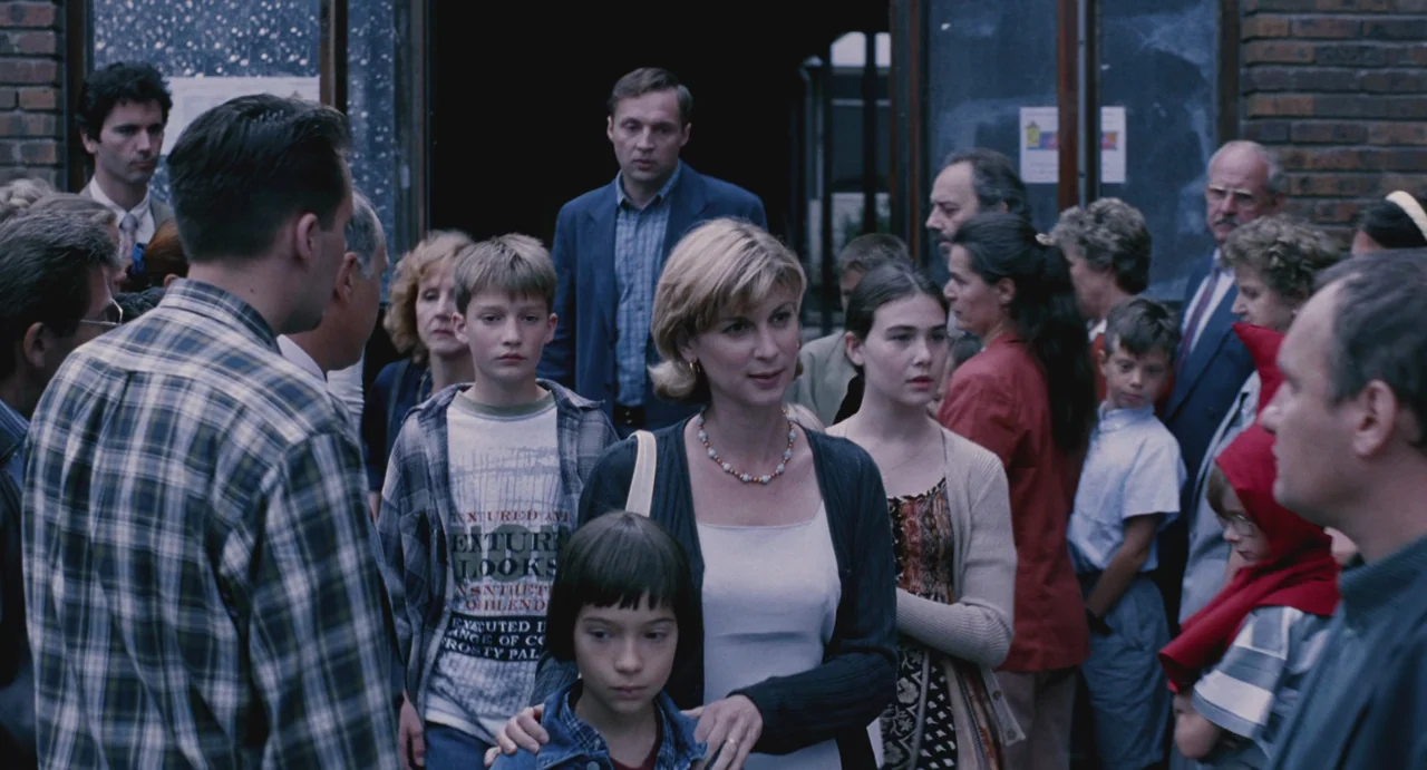 Ma Vie En Rose (1997) movie still: medium — A group of parents and children emerge from the brick entrance of a building. The diverse assembly…