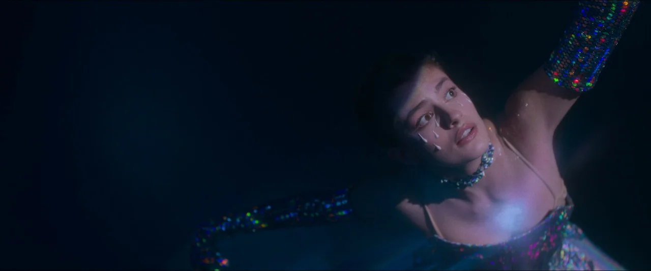 Birds of Paradise (2021) movie still: closeup — A dark stage environment surrounds a performer highlighted by a singular concentrated light. The…