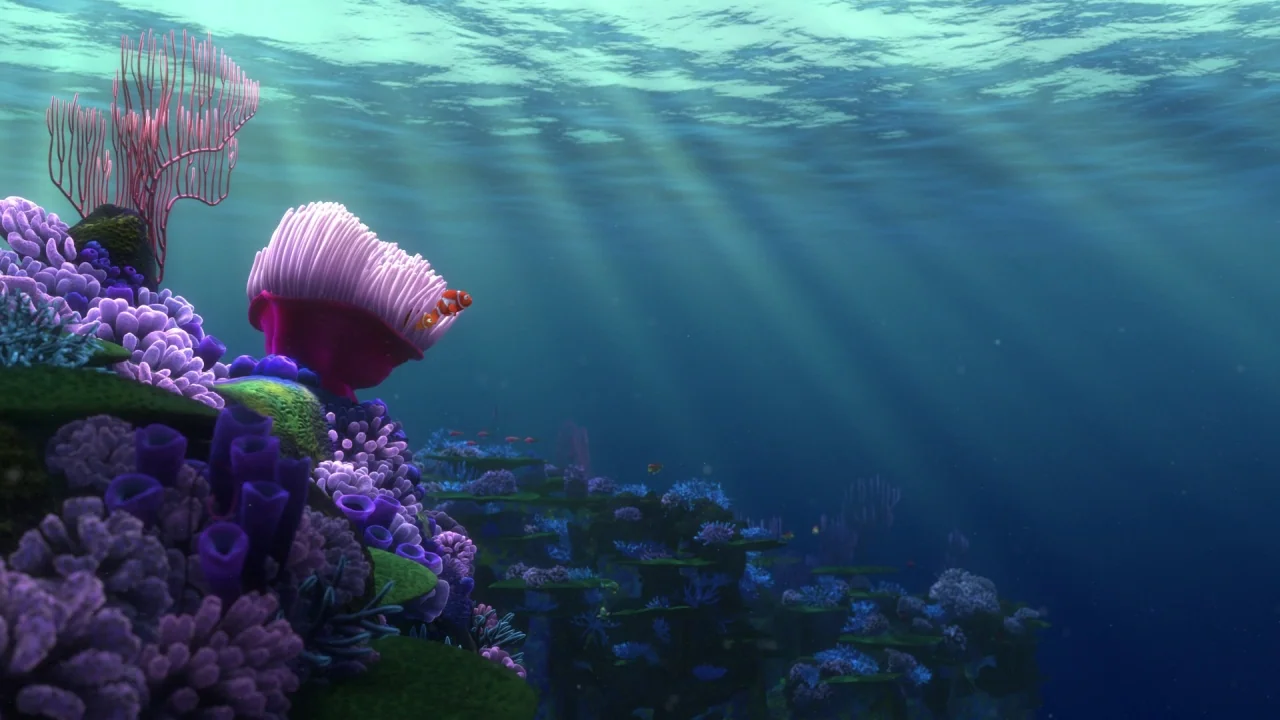 Finding Nemo (2003) movie still: wide — A vibrant coral reef extends across the sea floor under deep blue ocean water. Sunbeams filter through the…