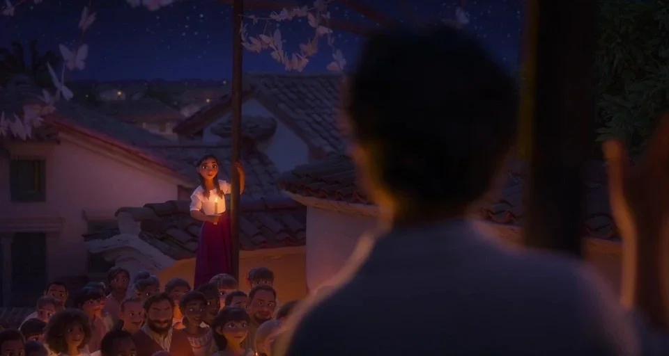 Encanto (2021) movie still: wide — A night scene shows a central female figure standing on a balcony overlooking a crowd. She holds a single lit…