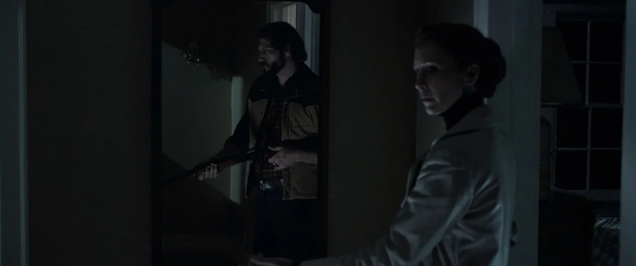 The Conjuring 2 (2016) movie still: medium — A dimly lit residential hallway at night features a large mirror on the wall. A woman stands in the…