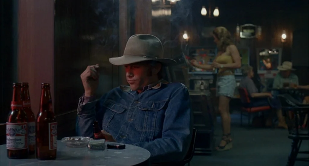 Brokeback Mountain (2005) movie still: medium — A dimly lit bar with wood-paneled walls and several patrons scattered throughout the background. A…