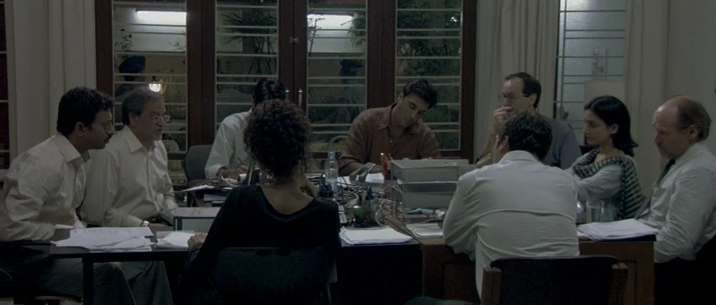 A Mighty Heart (2007) movie still: medium — A group of professionals sits around a table in a dimly lit, austere room. They are engaged in a…