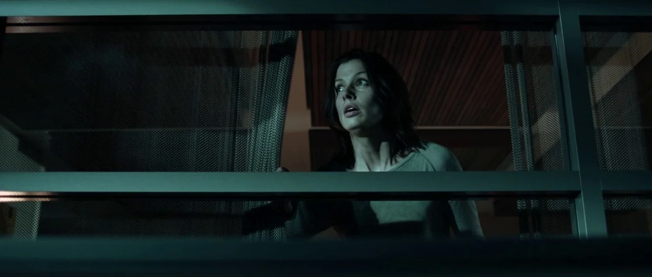 I, Robot (2004) movie still: medium — A dark interior space viewed through a segmented frame with metal mesh screens. A woman looks through the…