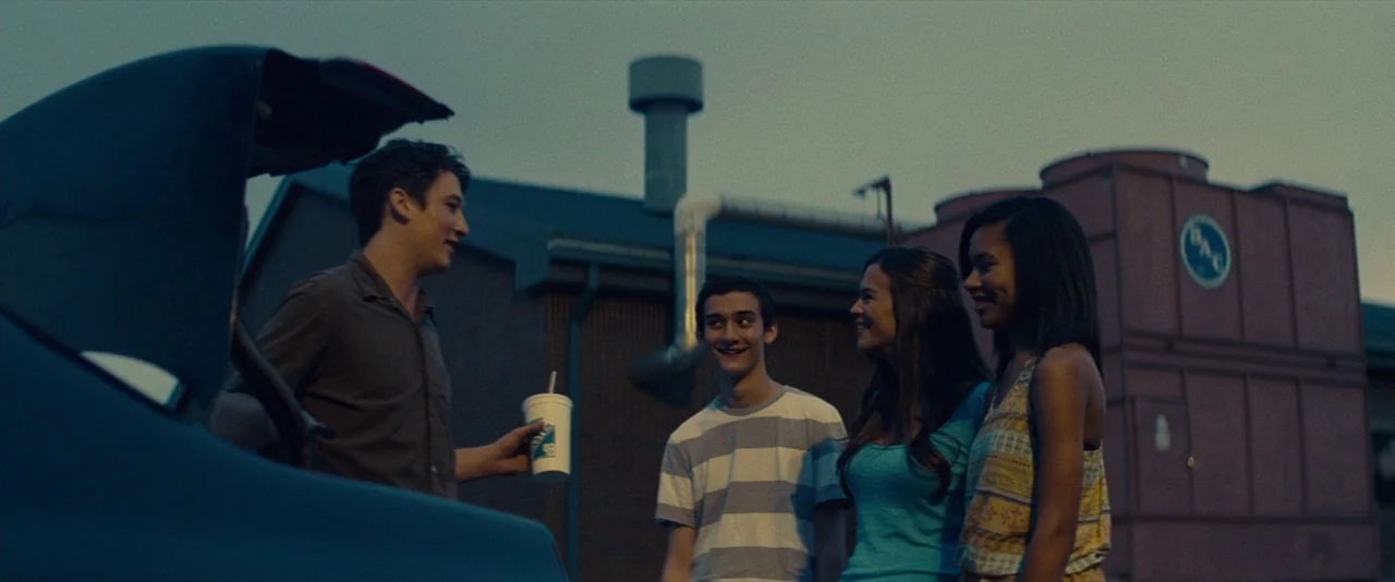 The Spectacular Now (2013) movie still: medium — A group of young people stands near an open car trunk in a parking lot. They are conversing in…