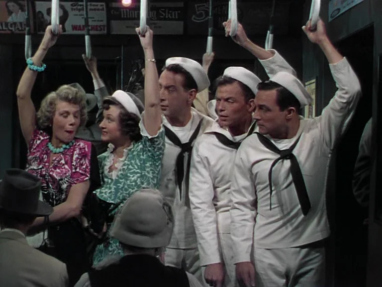 On The Town (1949) movie still: medium — A crowded subway car interior features posters visible on the ceiling paneling. Three sailors and two women…