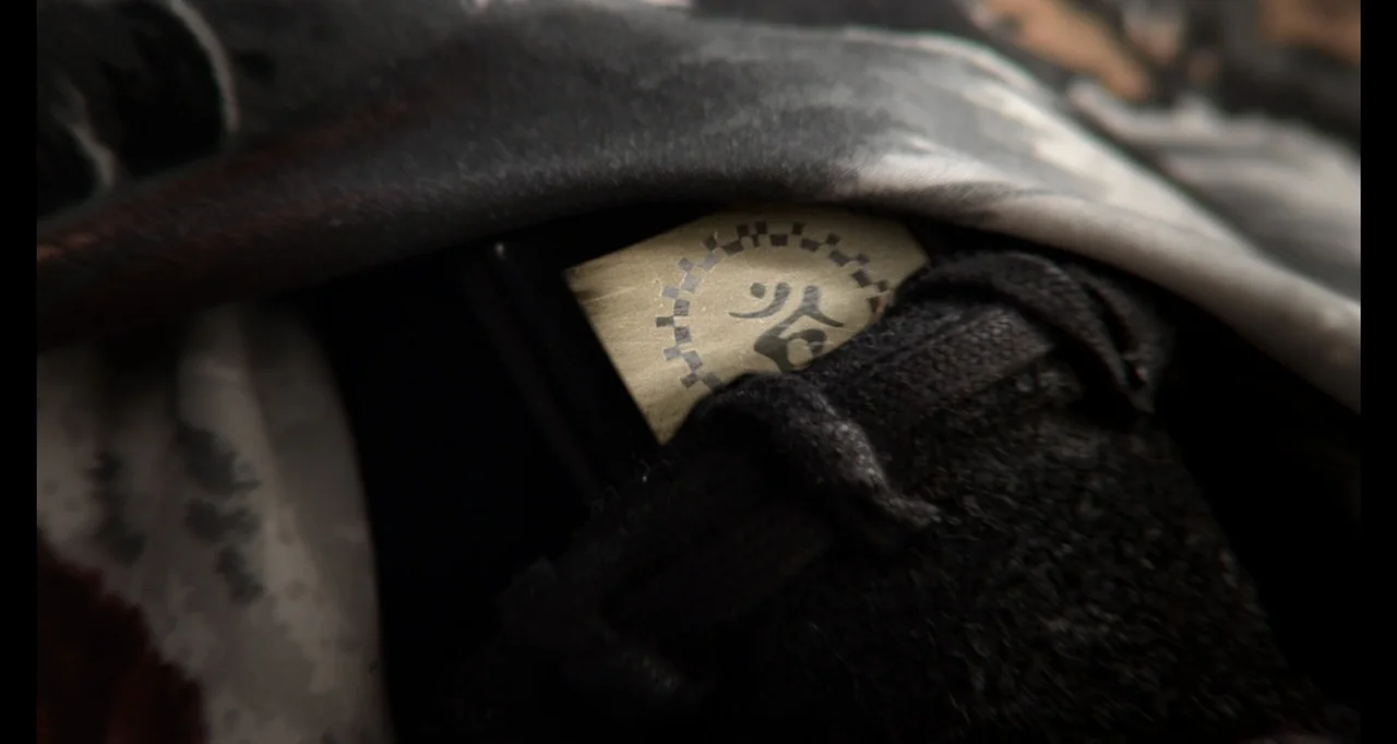 Ninja: Shadow of a Tear (2013) movie still: closeup — A close-up view shows a small rectangular tag featuring a gear and glyph icon. The tag is…