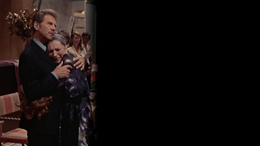 Day for Night (1973) movie still: medium — An interior space with a beige wall, wooden accents, and a striped chair. A man in a suit embraces a…