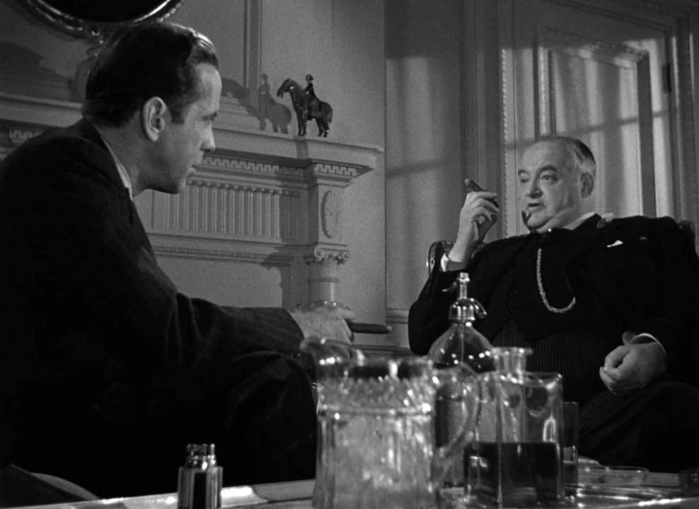 The Maltese Falcon (1941) movie still: medium — A dark, elegant room with architectural molding and a mantle featuring an equestrian statue. Two men…
