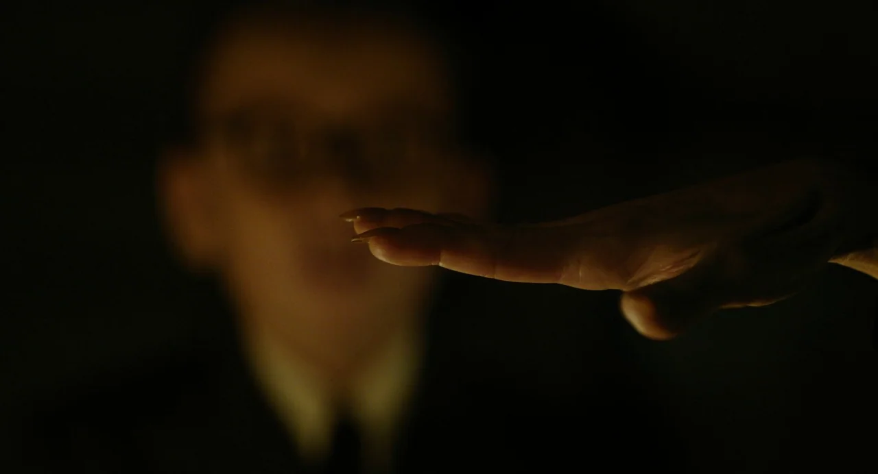 A Haunting In Venice (2023) movie still: closeup — A dimly lit environment provides no architectural context other than a solid black background. A…