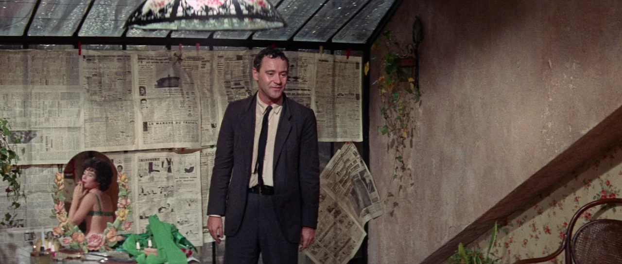 Irma La Douce (1963) movie still: fullbody — An attic room features a sloping glass ceiling and walls covered in newspapers. A man stands in the…