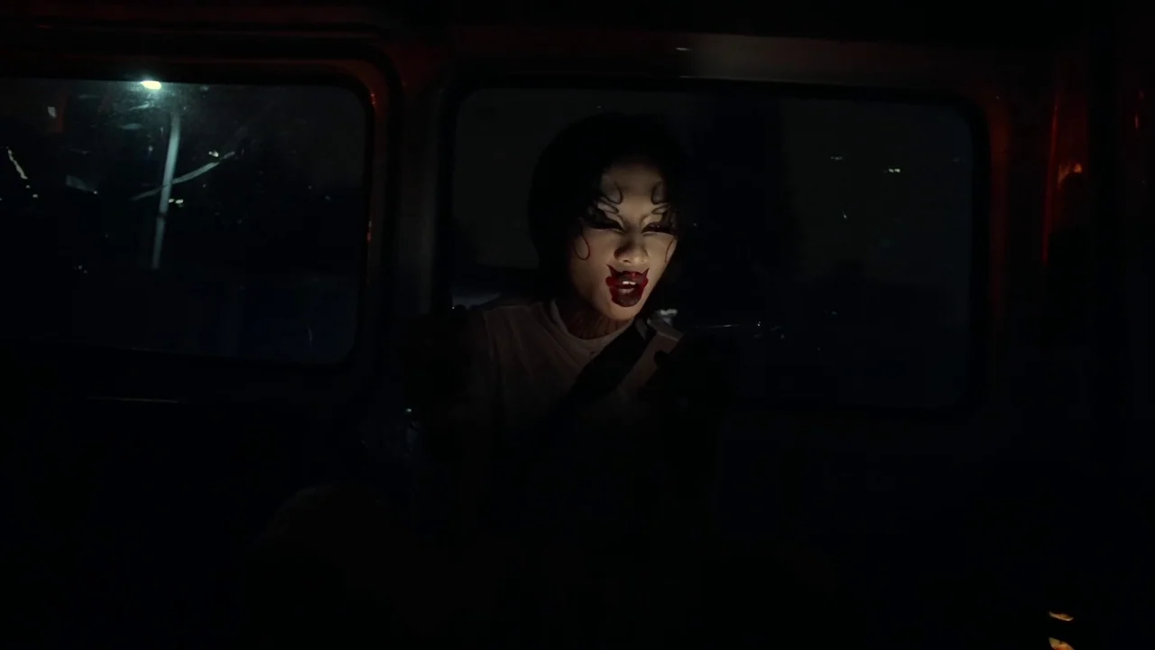 The Last Year of Darkness (2023) movie still: medium — Inside a dark vehicle at night, the subject sits in the passenger seat. The subject looks…