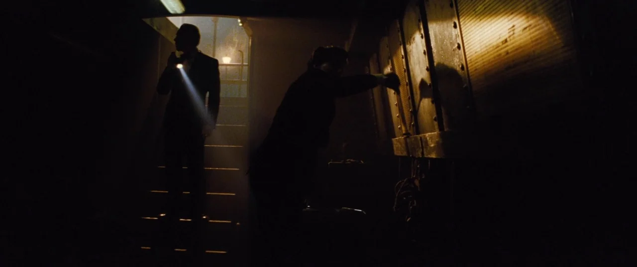 Mission: Impossible – Rogue Nation (2015) movie still: wide — An industrial space features a large metal storage tank and dimly lit staircase. Two…