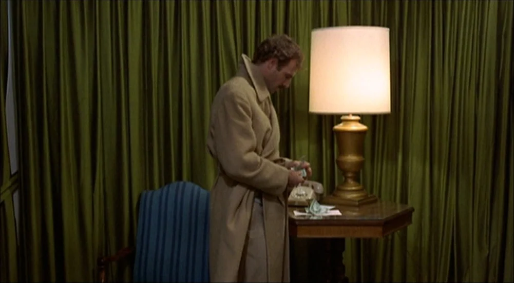 The King Of Marvin Gardens movie still: medium — A dimly lit room features floor-to-ceiling olive green curtains and a table with a lamp. A man…