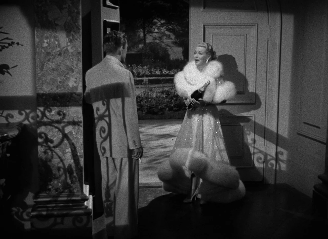 The Bad and the Beautiful (1952) movie still: fullbody — A dark foyer with an open door leads into a moonlit outdoor area. A woman in a fur stole…