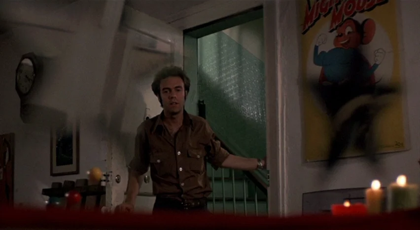 A Safe Place (1971) movie still: medium — A dimly lit apartment interior with a staircase visible through an open door. A man in a brown shirt…