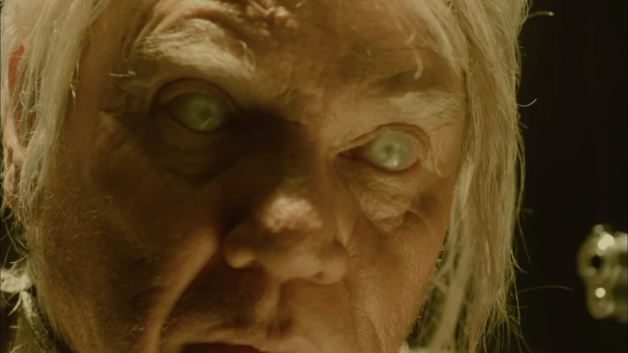 Silent Hill: Revelation 3D (2012) movie still: closeup — A dimly lit interior space contains an elderly man with pale, cloudy eyes. The man looks…