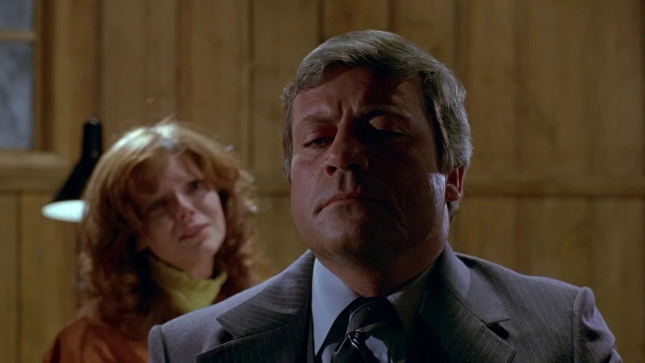 The Brood (1979) movie still: closeup — A man in a pinstripe suit stands in a wood-paneled room. He has his eyes closed while a woman watches him…