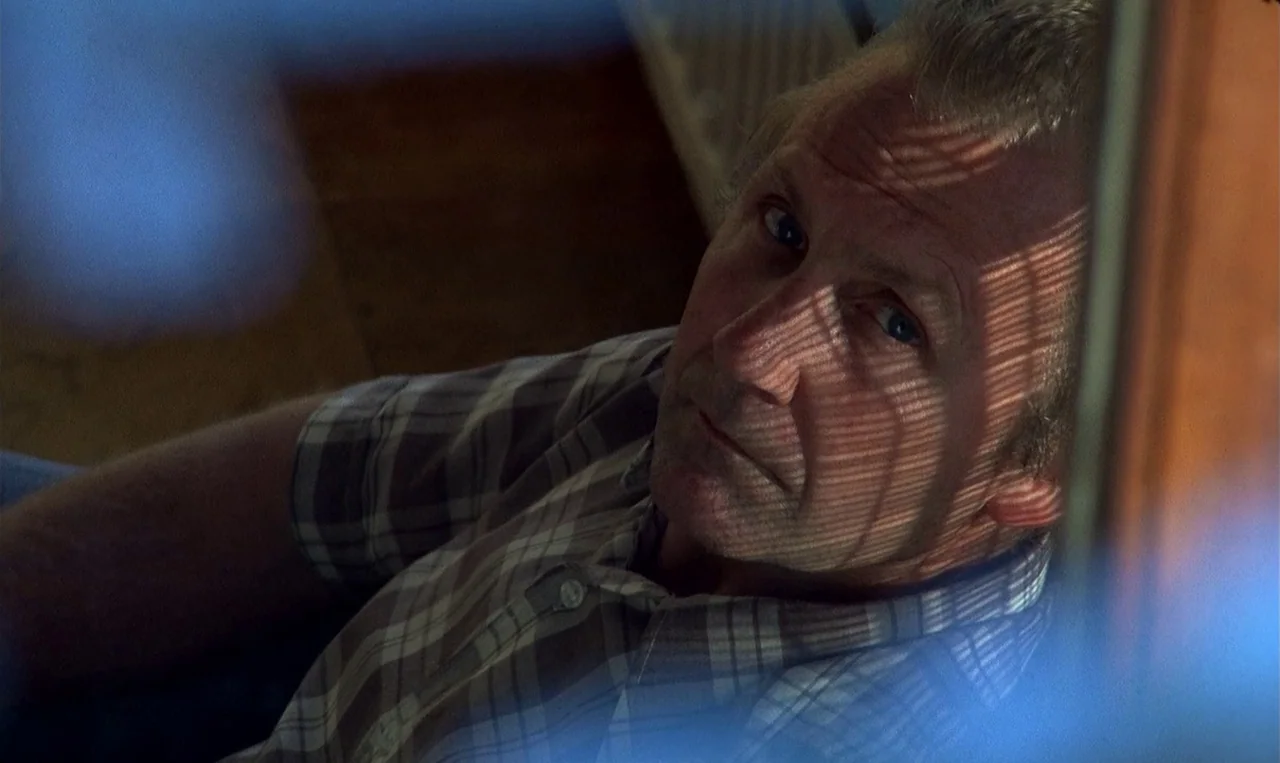 Man on the Roof (1976) movie still: closeup — A man's face is illuminated by light filtering through horizontal window blinds. He gazes upward at…