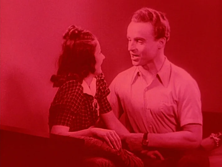 Innocence Unprotected (1968) movie still: medium — A man and a woman sit in a room with plain walls. They are engaged in conversation while looking…