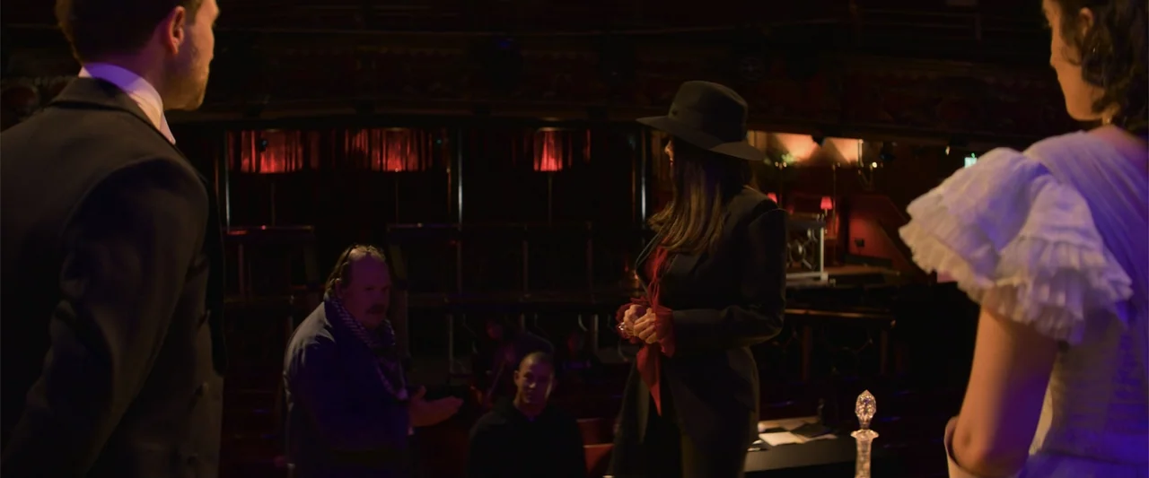 Magic Mike's Last Dance (2023) movie still: medium — A dark theater auditorium contains rows of seating and a dimly lit stage area. Four people…