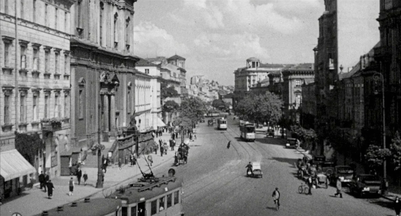 The Pianist (2002) movie still: establishing — A bustling urban boulevard in Warsaw features neoclassical stone architecture and multiple tram…