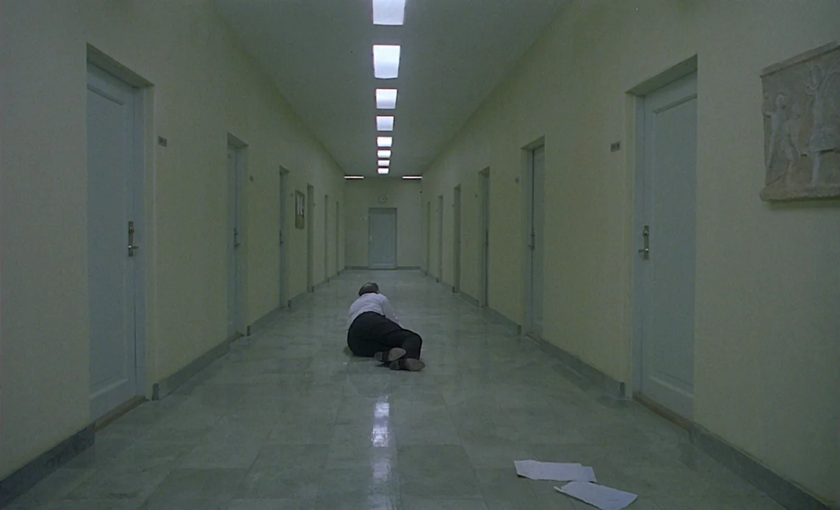 Songs from the Second Floor (2000) movie still: wide — A long, sterile corridor with pale yellow walls features many identical closed white doors. A…