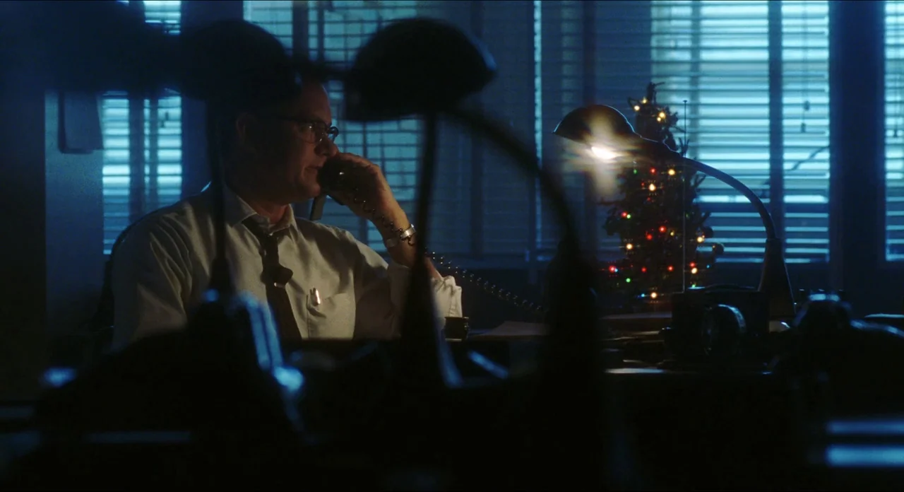 Catch Me If You Can (2002) movie still: medium — A cluttered dark office at night features window blinds and a small decorated Christmas tree. A man…