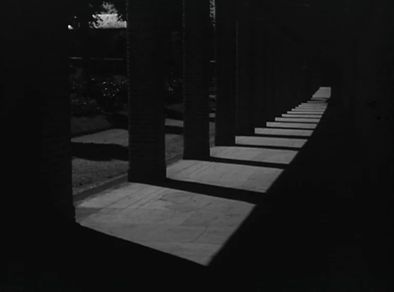 Head Against The Wall (1959) movie still: establishing — A stone colonnade features a long row of pillars casting angled shadows onto the ground.…