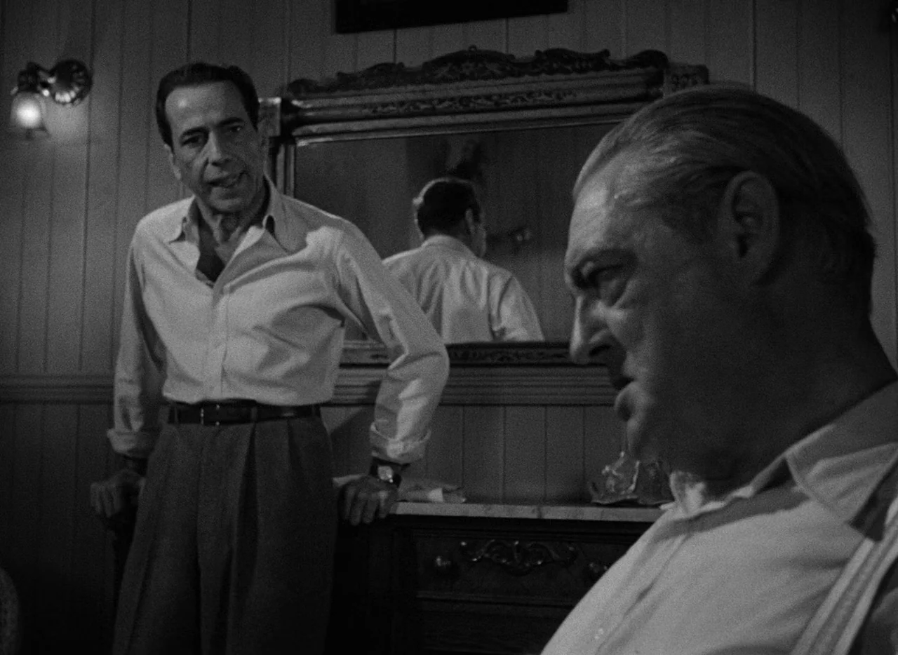Key Largo (1948) movie still: medium — A dark bedroom features paneled walls and an ornate mirror reflecting one man. Two men in collared shirts…