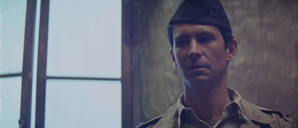Catch 22 (1970) movie still: medium — A dimly lit room features a window with a simple wood frame. A man in a vintage military uniform stands in…