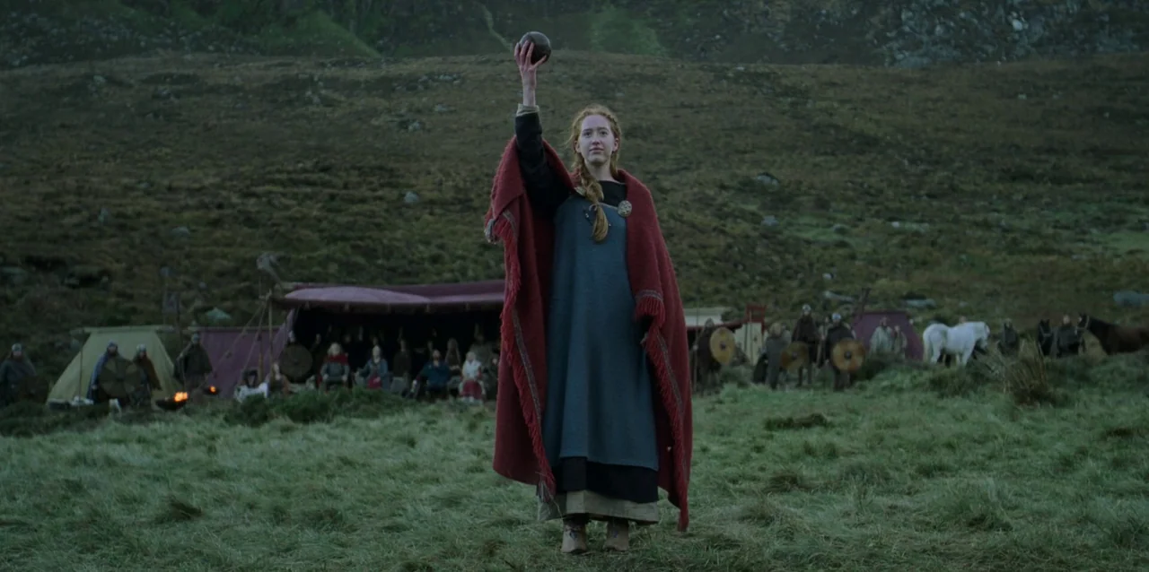 The Northman (2022) movie still: fullbody — A hilly, grassy highland landscape features a small encampment with tents in the background. A woman in…