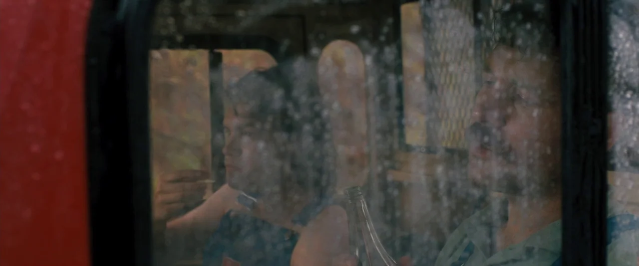 Prince Avalanche (2013) movie still: medium — A truck cabin interior is viewed through a rain-covered window during a day. Two men sit side by side…
