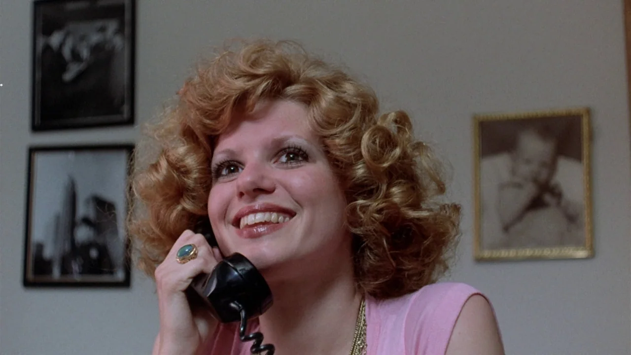 The Sentinel (1977) movie still: closeup — A light-colored interior wall features three framed pictures hanging in the background. A woman with…