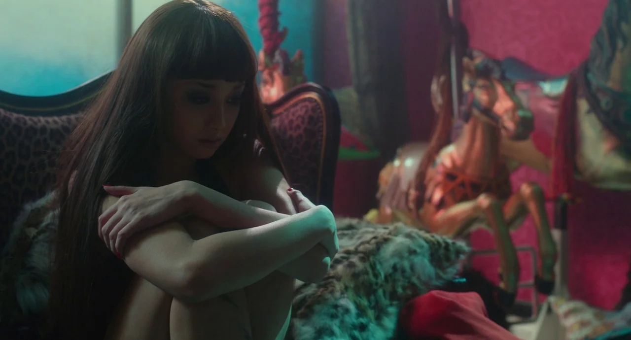 Helter Skelter (2012) movie still: medium — A dimly lit room features hot pink wallpaper and leopard print fabric cushions. A woman with long brown…