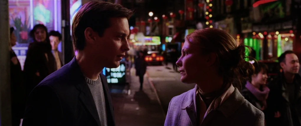 Spider-Man 2 (2004) movie still: medium — A nighttime city street features blurred neon signs in the background with indistinct pedestrians. A man…